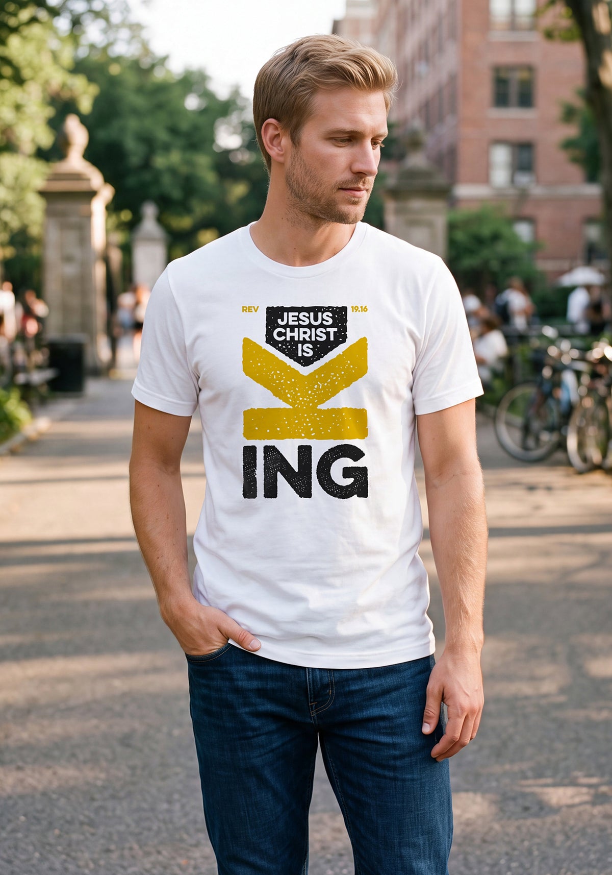 Man standing in an urban park wearing a white t-shirt with Revelation 19.16 graphic printed on the front.