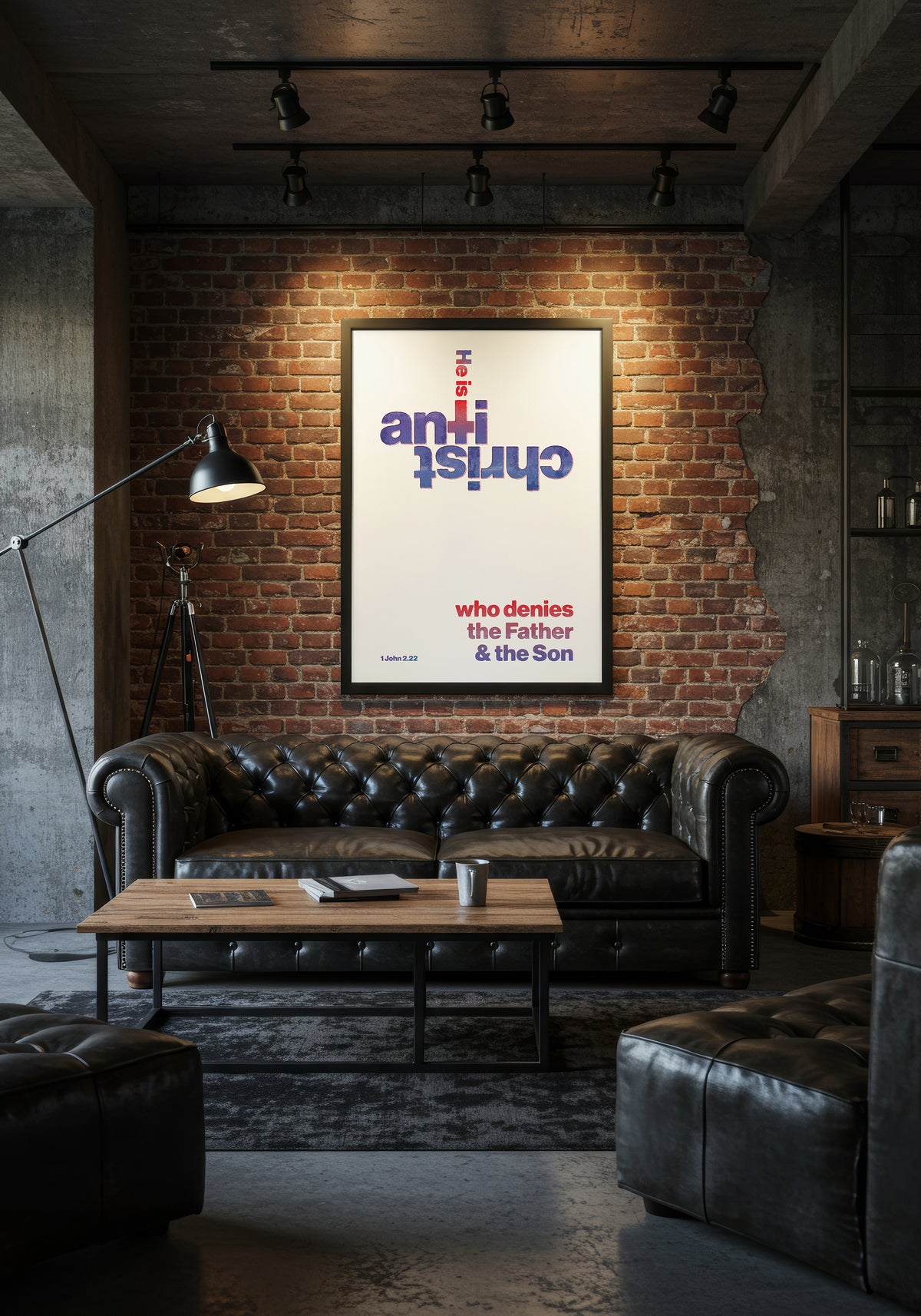 1 John 2:22 print in a black frame, styled above a black leather Chesterfield sofa in an industrial living room.