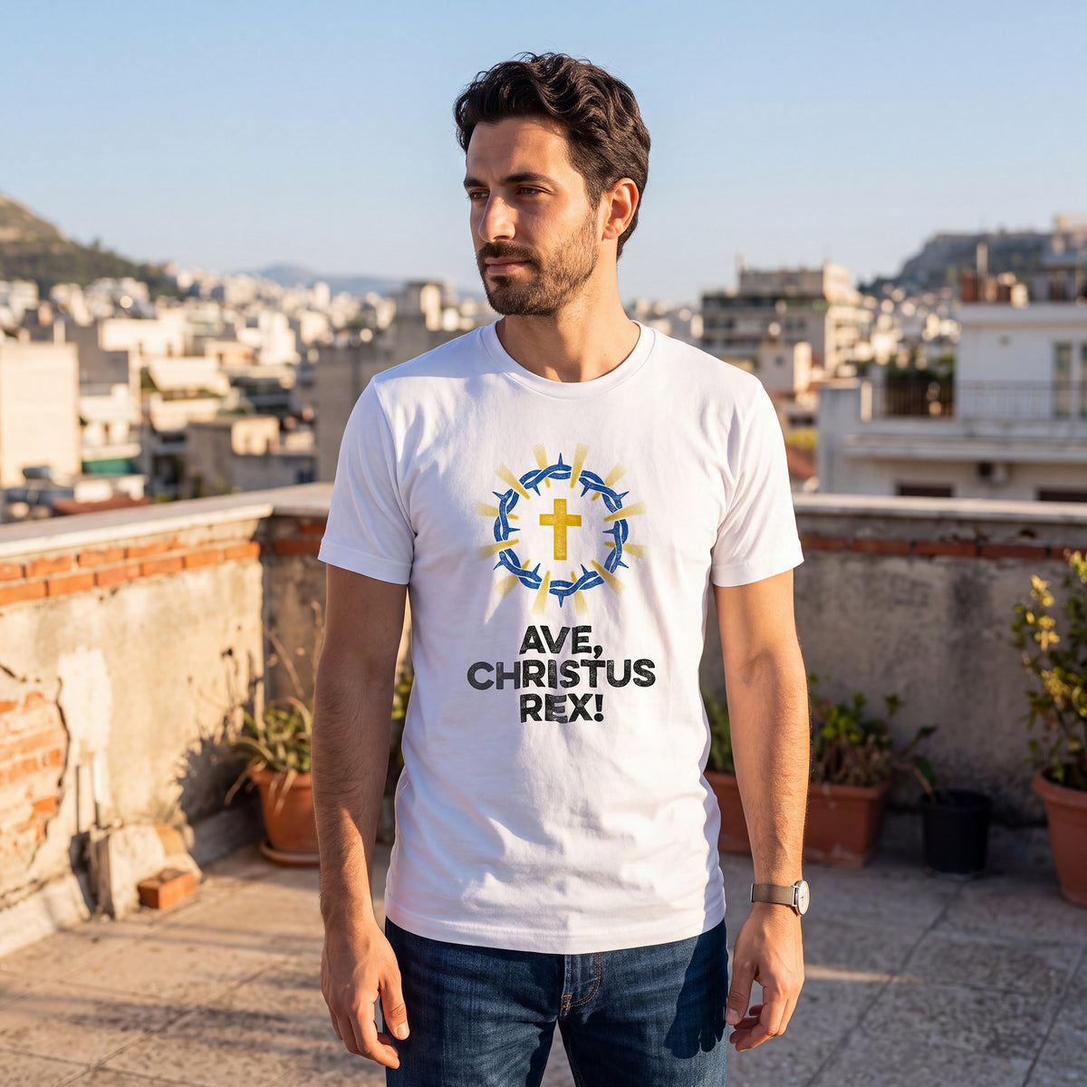 Man on rooftop terrace with cityscape, wearing white t-shirt with Ave Christus Rex graphic print.