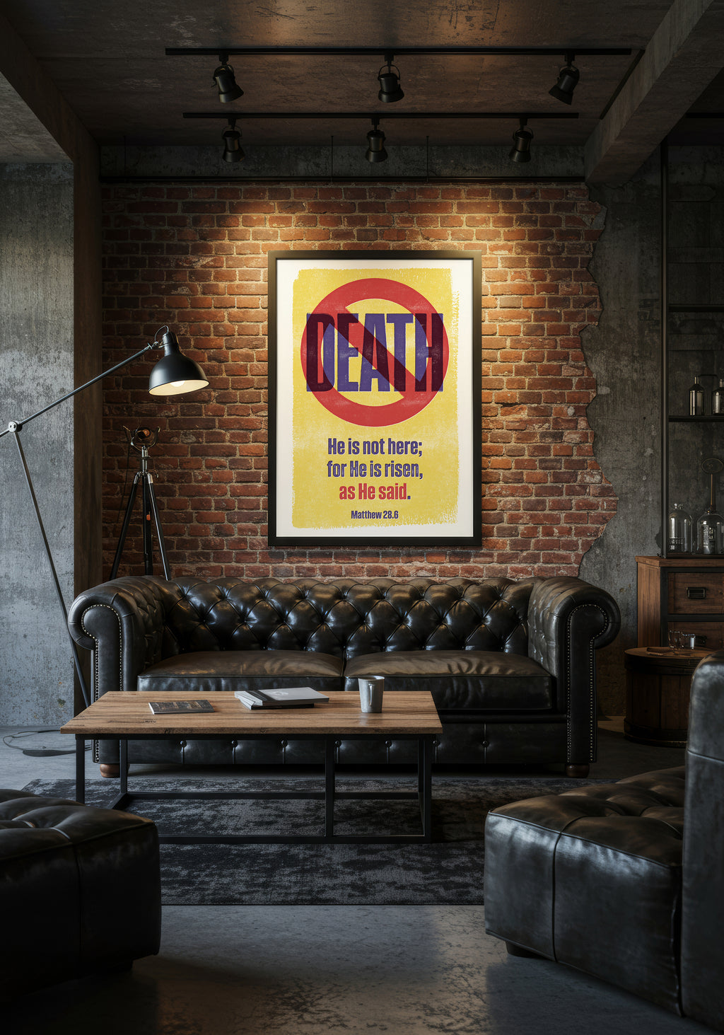 Matthew 28:6 print in a black frame, styled above a black leather Chesterfield sofa in an industrial living room.