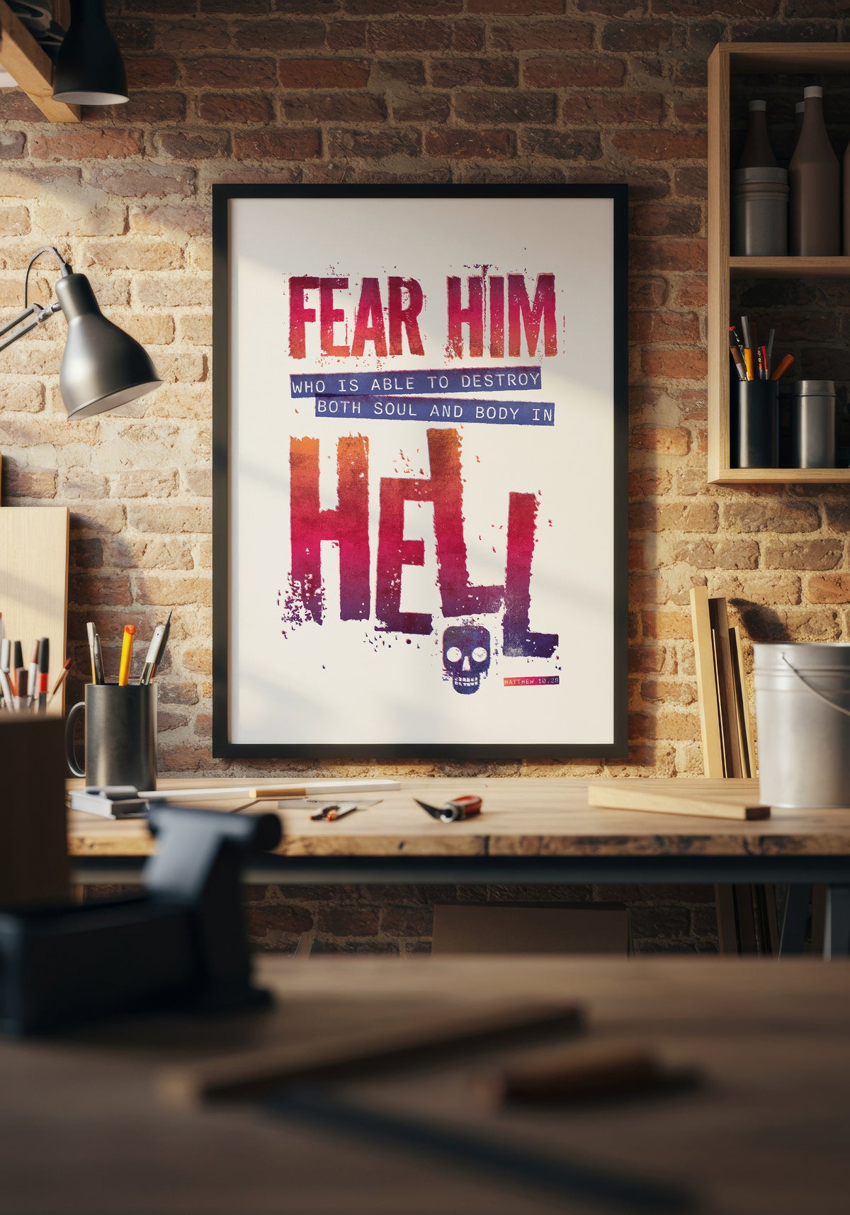 Matthew 10:28 print in a black frame, lit by natural sunlight above a workbench in a home workshop.