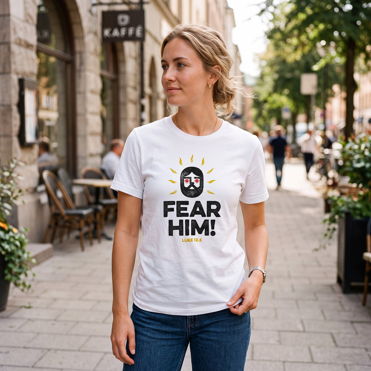Woman on city sidewalk wearing white t-shirt with Luke 12:5 graphic print.