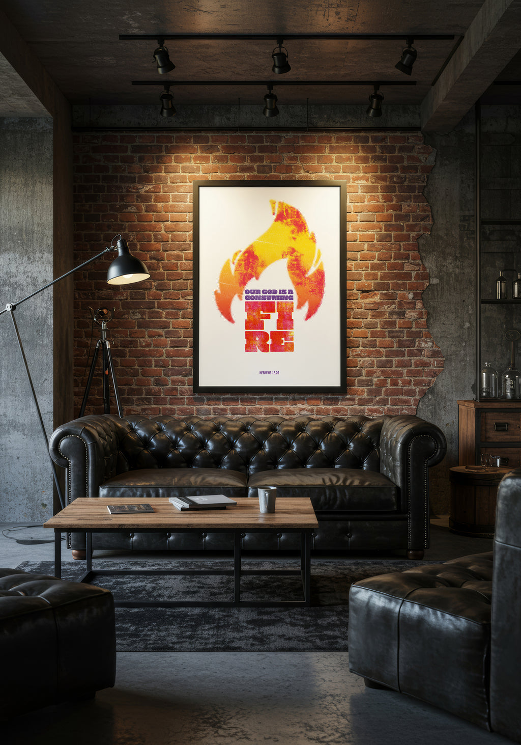 Hebrews 12:29 art print in a black frame, hung above a black leather Chesterfield sofa in an industrial living room.
