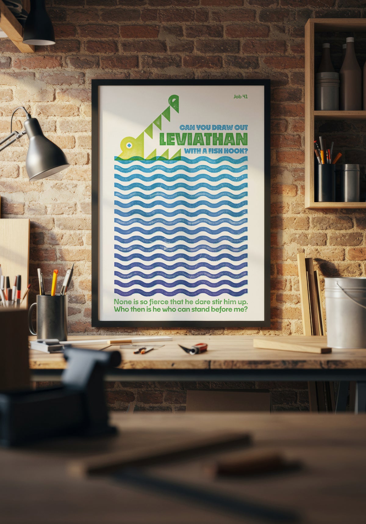 Job 41 scripture art print with a blue and green leviathan illustration in a black frame above a sunlit workbench.