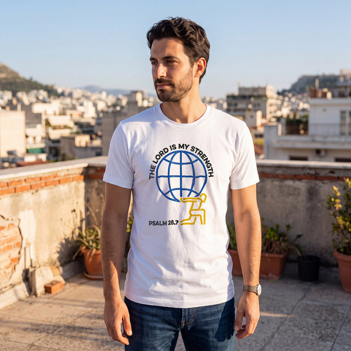 Man standing on a rooftop terrace with a cityscape background, wearing a white t-shirt with Psalm 28:7 graphic printed on the front.