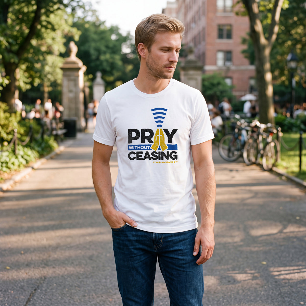 Man standing in an urban park wearing a white t-shirt with 1 Thessalonians 5:17 graphic printed on the front.