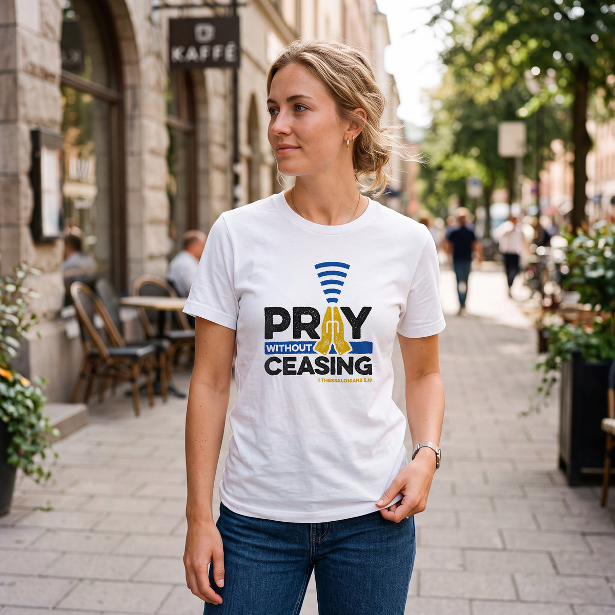 Woman on city sidewalk wearing white t-shirt with 1 Thessalonians 5:17 graphic print.