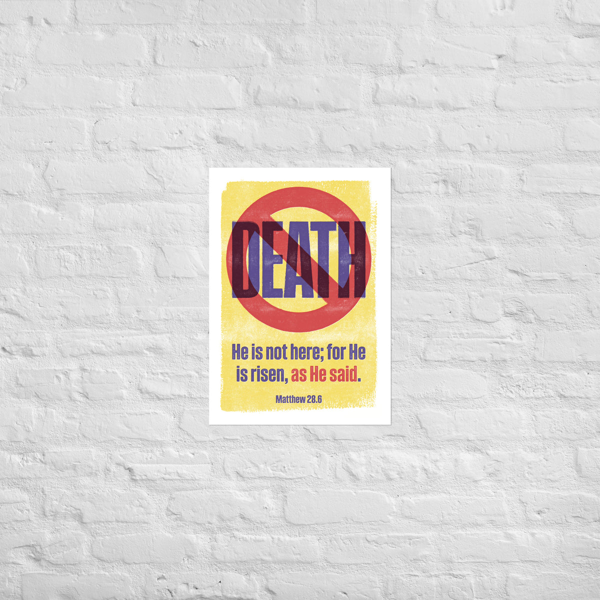 Matthew 28:6 print mounted directly on a white brick wall for a frameless, modern look.